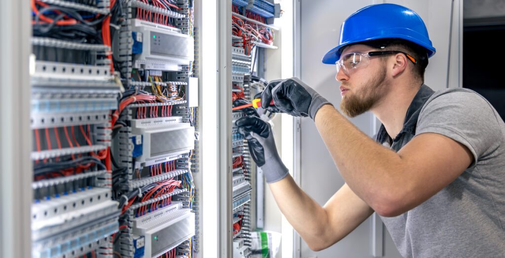 Male electrician in uniform working in a switchboard. Electricity. High quality photo. Male electrician in hard hat. A male electrician solves a problem with electricity.